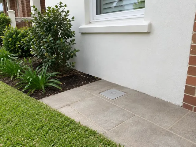 Flush capped access cover in paved patio beside white wall and garden in Wahroonga